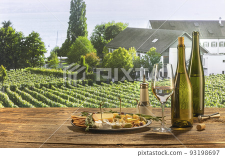 Delicious white wine standing on wooden table. Yummy and romantic breakfast. Appetizers with cheese, honey, grapes and crackers. Summer vineyard landscape view 93198697