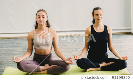 Two Caucasian women exercise doing the yoga pose stretching at home, healthy lifestyle concept Two Caucasian women exercise doing the yoga pose stretching at home, healthy lifestyle concept 93199890