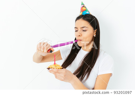 Portrait young woman in birthday cap looking aside blowing pipe 93201097