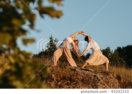 Young Adult Couple Making Beautiful Pose, Man and Woman Practicing Yoga Outdoors on the Rocky Hill at Sunset 93201533