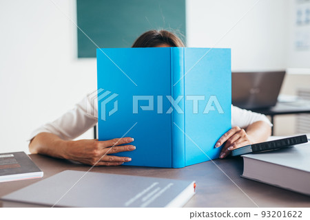 Young woman sitting by table and reading book. 93201622