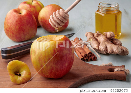 Preparing apples for baking in the oven. A drop of honey flows from a spoon onto an apple on a cutting board 93202073