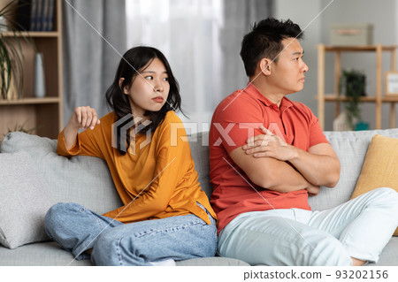 Young asian woman looking at her angry husband, home interior Young asian woman looking at her angry husband, home interior 93202156