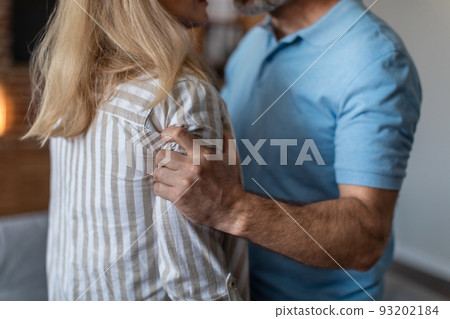 Aggressive nervous angry adult caucasian husband holds and threatens to wife in living room interior, cropped Aggressive nervous angry adult caucasian husband holds and threatens to wife in living room interior, cropped 93202184