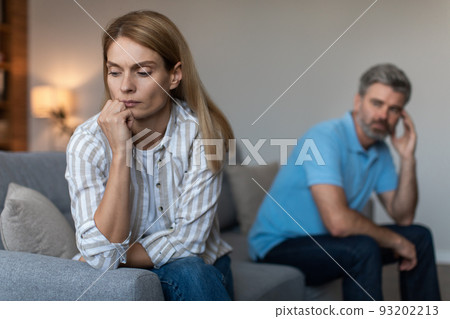 Unhappy depressed mature caucasian husband with beard ignores offended wife in living room interior 93202213
