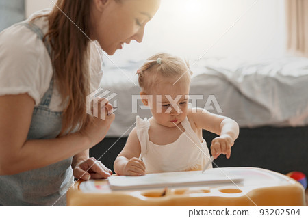 Little smiling girl painting with her mother at home while spending time together Little smiling girl painting with her mother at home while spending time together 93202504