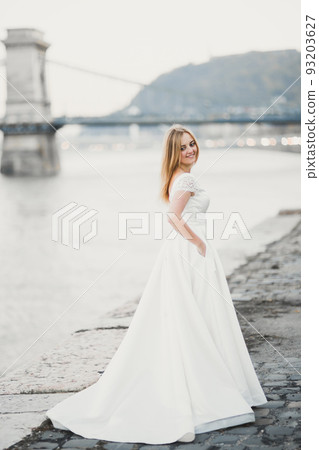 Beautiful brunette bride in elegant white dress holding bouquet posing near river 93203627