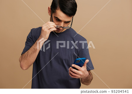 handsome man with a phone in hand in a gray T-shirt and glasses tin hands beige background handsome man with a phone in hand in a gray T-shirt and glasses tin hands beige background 93204541
