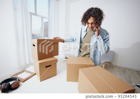 guy with curly hair with a phone in hand with boxes moving Lifestyle guy with curly hair with a phone in hand with boxes moving Lifestyle 93204543
