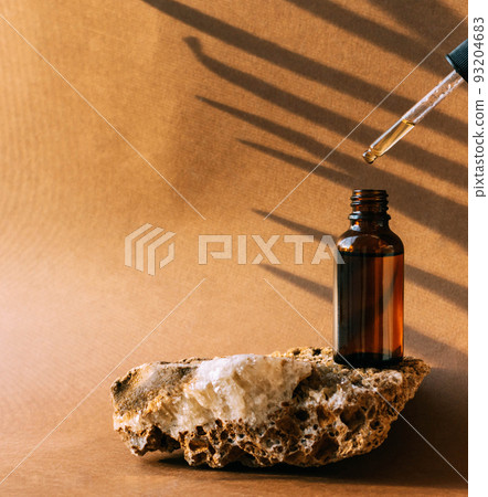 A bottle with a pipette made of dark amber glass, a cosmetic product on a stone podium pedestal A bottle with a pipette made of dark amber glass, a cosmetic product on a stone podium pedestal 93204683