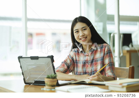 Young asian woman study in front of the laptop computer and and using headphones at offsite.. Young asian woman study in front of the laptop computer and and using headphones at offsite.. 93208736