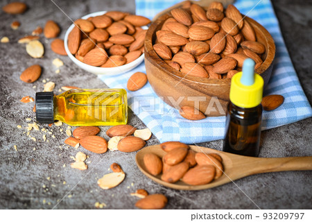 Almond oil and Almonds nuts on bowl dark background, Delicious sweet almonds oil in glass bottle, roasted almond nut for healthy food and snack organic vegetable oils for cooking or spa 93209797