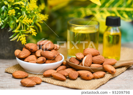 Almond oil and Almonds nuts on bowl plant green nature background, Delicious sweet almonds oil in glass bottle, roasted almond nut for healthy food and snack organic vegetable oils for cooking or spa 93209798