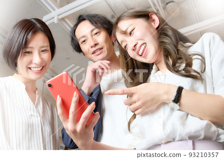 Three men and women who talk while looking at the screen of the smartphone 93210357