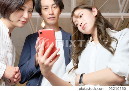 Three men and women who talk while looking at the screen of the smartphone Three men and women who talk while looking at the screen of the smartphone 93210360
