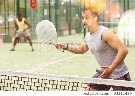 Athletic mens plays padel. View through tennis net 93211420