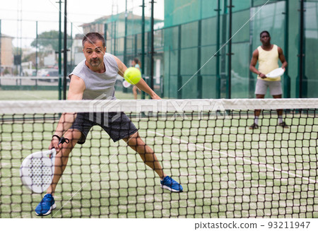 Athletic mens plays padel. View through tennis net 93211947