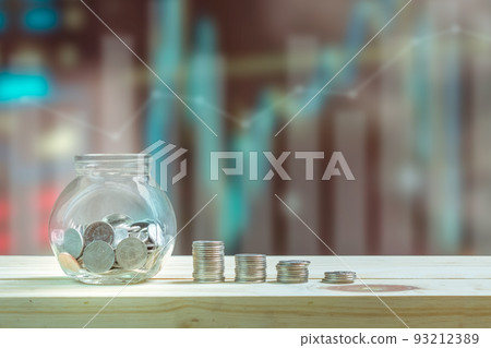 Saving money and investment concept, Coins in glass bottle for savings and stack coins to show increase of savings money on wooden table, graphs and index blurred background. 93212389