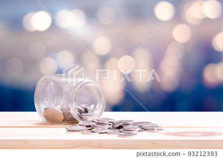 Concept saving and financial with coins spilling out of a glass bottle on wooden table and bokeh background. 93212393