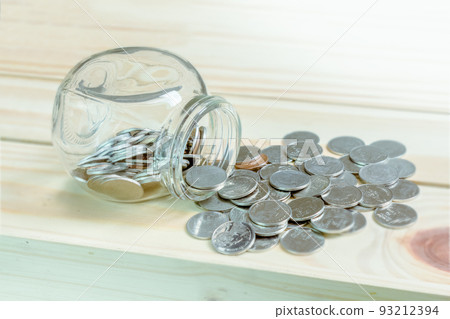 Concept saving and financial with coins spilling out of a glass bottle on wooden table. Concept saving and financial with coins spilling out of a glass bottle on wooden table. 93212394