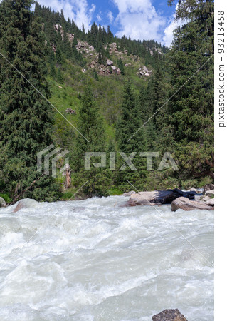 A beautiful stormy mountain river of milky hue flows rapidly among large stones and boulders near the mountains and the blue sky. The mountain river fascinates and attracts attention. A beautiful stormy mountain river of milky hue flows rapidly among large stones and boulders near the mountains and the blue sky. The mountain river fascinates and attracts attention. 93213458