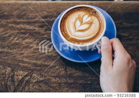 Cropped shot view of human hand with a cup of hot coffee latte. 93216388