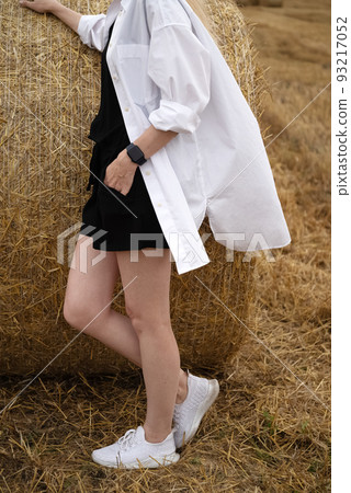 Young woman stand next to rolled stack of straw in field, summer crop season Young woman stand next to rolled stack of straw in field, summer crop season 93217052