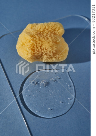 A natural sponge and a drop of gel or shampoo on a blue background. 93217311