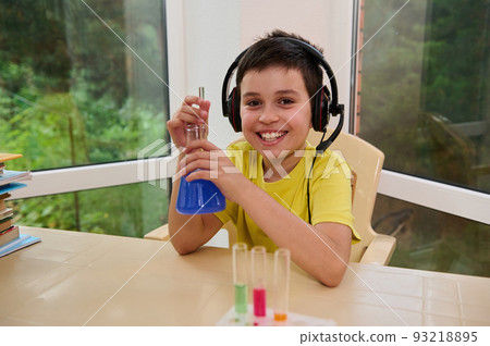 Portrait of smiling, inspired child chemist, schoolboy using a glass stick mixes chemicals in the flat-bottomed flask, while conducting experiments in the chemistry lesson. Science, education. school Portrait of smiling, inspired child chemist, schoolboy using a glass stick mixes chemicals in the flat-bottomed flask, while conducting experiments in the chemistry lesson. Science, education. school 93218895