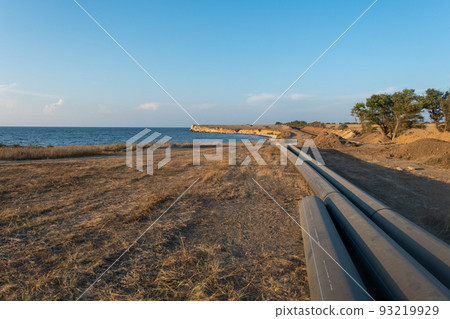 Pipes for laying water pipes lie on the lawn. Sunset, the rays of the sun illuminate the construction site Pipes for laying water pipes lie on the lawn. Sunset, the rays of the sun illuminate the construction site 93219929
