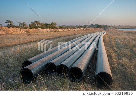 Pipes for laying water pipes lie on the lawn. Sunset, the rays of the sun illuminate the construction site 93219930