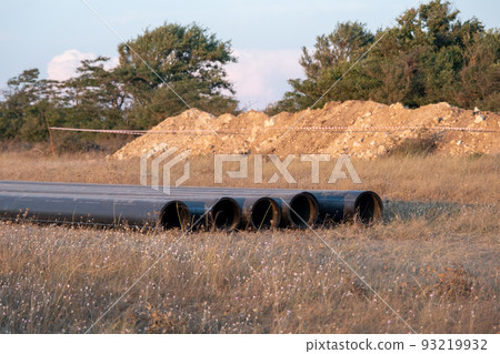 Pipes for laying water pipes lie on the lawn. Sunset, the rays of the sun illuminate the construction site Pipes for laying water pipes lie on the lawn. Sunset, the rays of the sun illuminate the construction site 93219932
