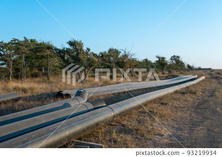 Pipes for laying water pipes lie on the lawn. Sunset, the rays of the sun illuminate the construction site 93219934