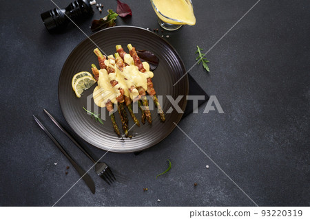baked aspargus covered with bacon on a black ceramic plate baked aspargus covered with bacon on a black ceramic plate 93220319