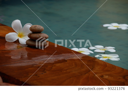 Stack of flat stones with a frangipani flower beside a swimming pool 93221376
