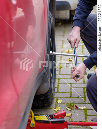 A wrench in the hands of an auto mechanic unscrews the bolts and nuts of a car wheel. Autumn day. A wrench in the hands of an auto mechanic unscrews the bolts and nuts of a car wheel. Autumn day. 93221762