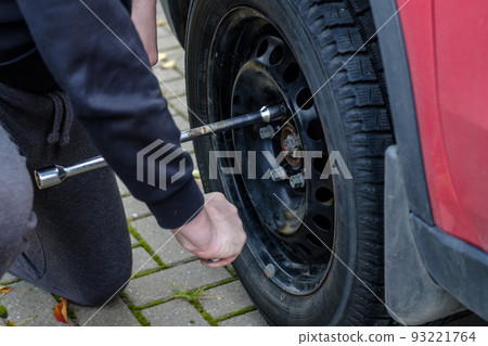 A wrench in the hands of an auto mechanic unscrews the bolts and nuts of a car wheel. Autumn day. A wrench in the hands of an auto mechanic unscrews the bolts and nuts of a car wheel. Autumn day. 93221764