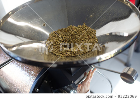 Coffee roaster machine at coffee roasting process. Young woman worker barista load green coffee beans in apparatus. Coffee roaster machine at coffee roasting process. Young woman worker barista load green coffee beans in apparatus. 93222069