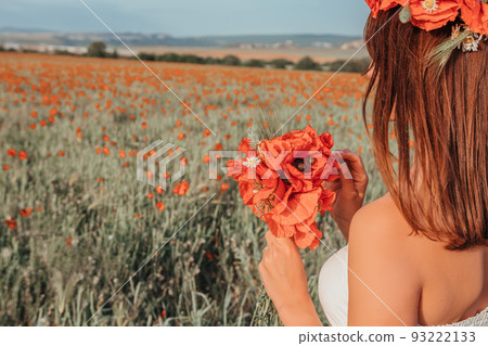 Bride in a white dress holding a bouquet of poppy flowers, warm sunset time on the background of the red poppy field. Copy space. The concept of calmness, silence and unity with nature. 93222133