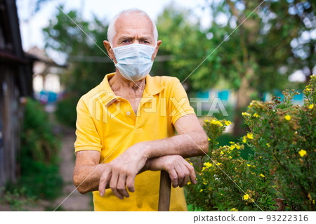 Senior man in mask with shovel standing in yard of his house Senior man in mask with shovel standing in yard of his house 93222316