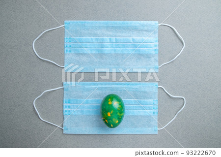 One green easter egg lies on a blue medical mask on a gray background. One green easter egg lies on a blue medical mask on a gray background. 93222670