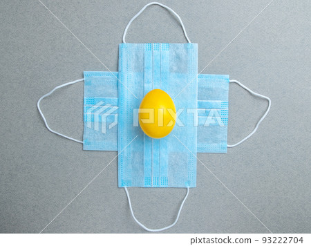 Yellow easter egg lies on blue medical masks on a gray background. Yellow easter egg lies on blue medical masks on a gray background. 93222704