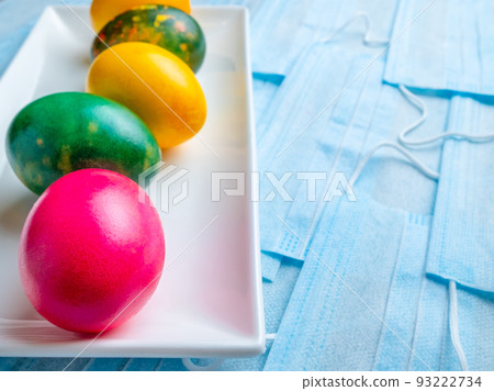 Colored Easter eggs on a white plate on a background of blue medical masks. Colored Easter eggs on a white plate on a background of blue medical masks. 93222734