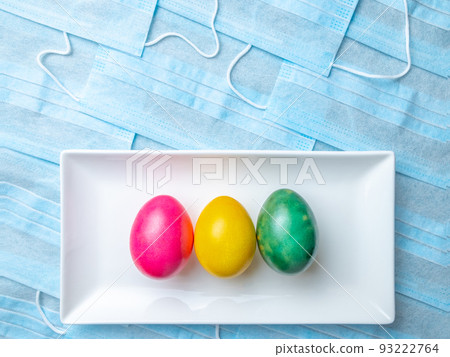 Colored Easter eggs on a white plate on a background of blue medical masks. Colored Easter eggs on a white plate on a background of blue medical masks. 93222764