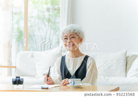 Senior woman writing a letter in the living room 93223568