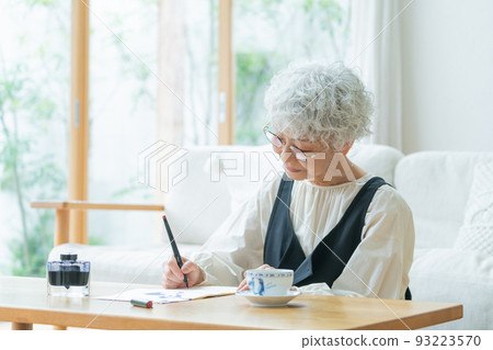 Senior woman writing a letter in the living room 93223570