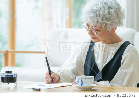 Senior woman writing a letter in the living room Senior woman writing a letter in the living room 93223572