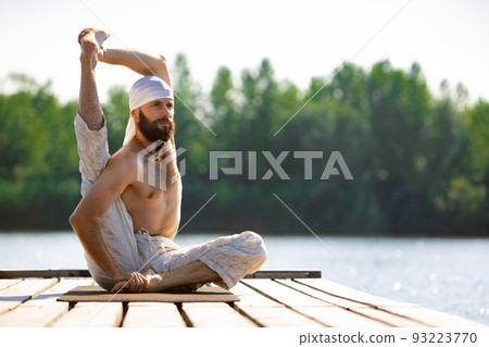 Young man practicing yoga on river berth at sunrise, outdoors. Self awareness and acceptance. Concept of mental health, relaxation, harmony with nature Young man practicing yoga on river berth at sunrise, outdoors. Self awareness and acceptance. Concept of mental health, relaxation, harmony with nature 93223770