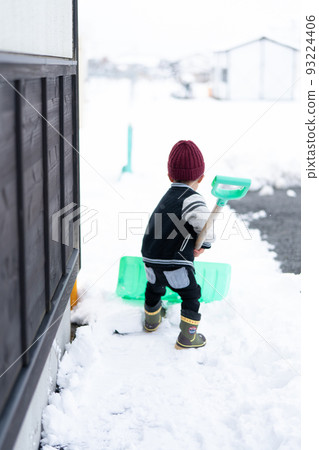 A back view of a boy who works hard to shovel snow with a shovel 93224406