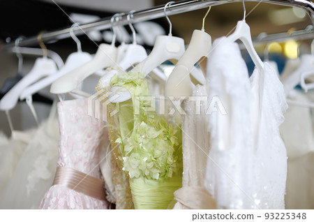 Few beautiful dresses on a hanger in wedding salon or atelier sewing studio. Wedding exhibition or shop, evening and bridesmaid dresses. Holiday clothes rental 93225348